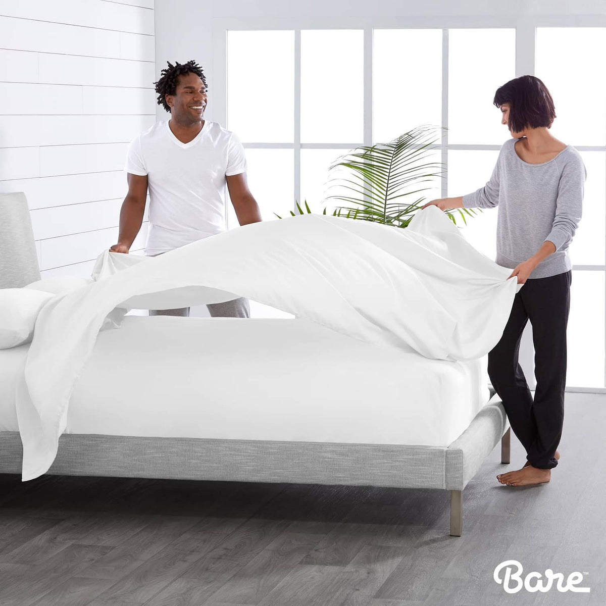 White flat sheet set being fitted on a bed with two people adjusting sheets