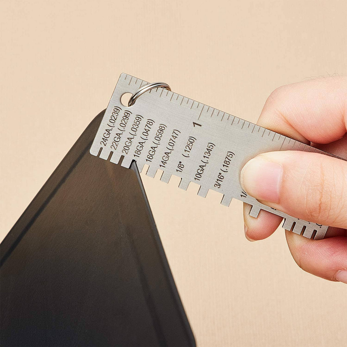 Wire thickness gauge held by hand, measuring metal sheet thickness with numbered tabs