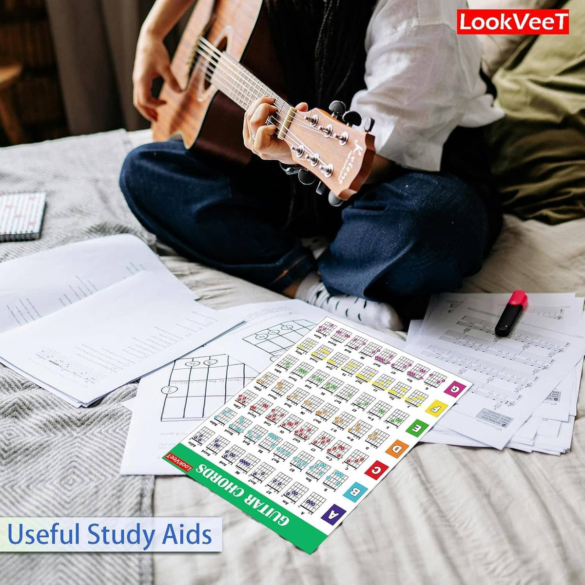 Guitar chord chart poster and printed study sheets on a bed during practice
