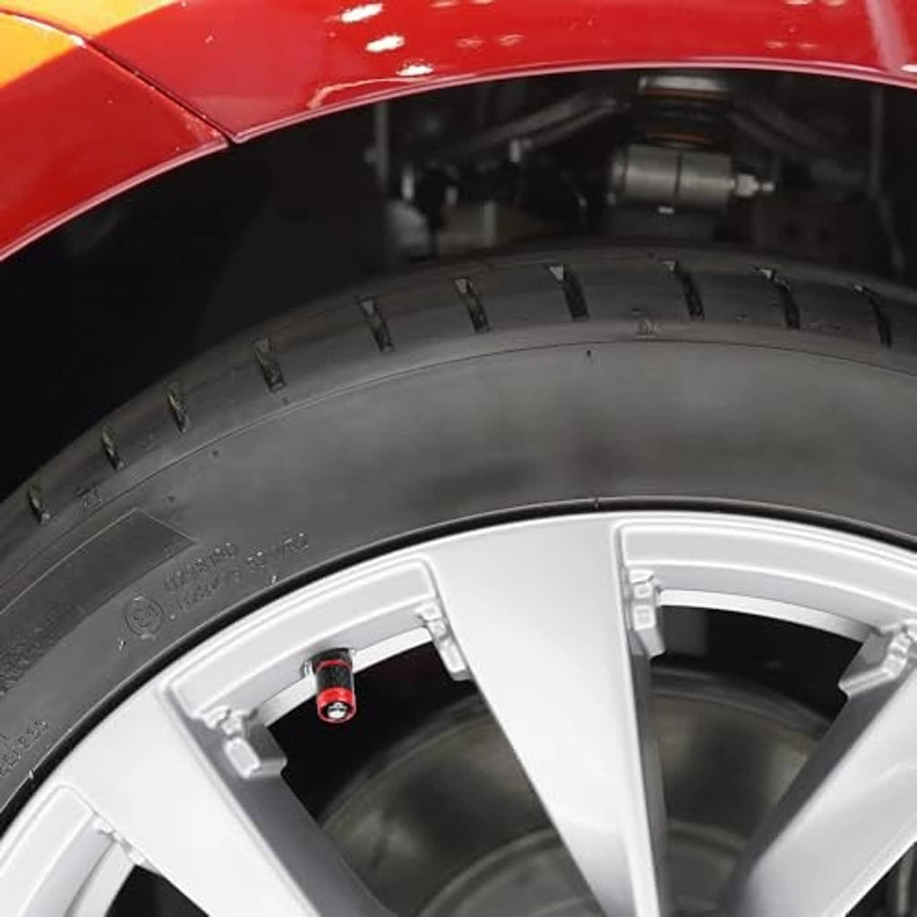 Red carbon fiber tire valve cap with skull emblem installed on a white wheel rim.