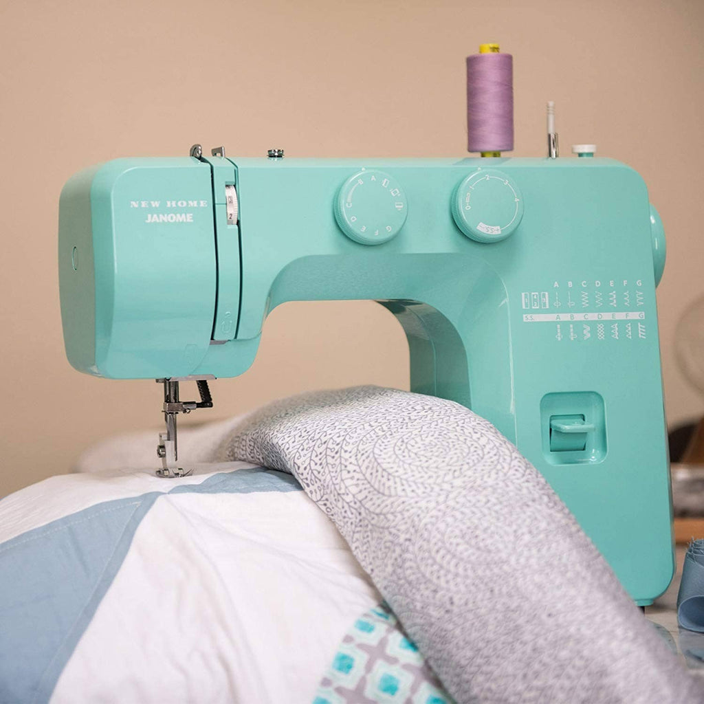 Turquoise sewing machine stitching on folded fabric with thread spool on top