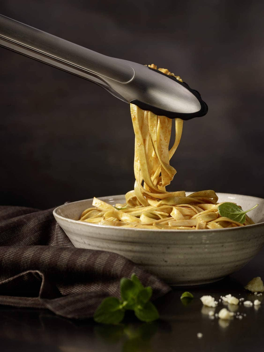 Silver locking tongs lifting pasta; black silicone tips grip food securely