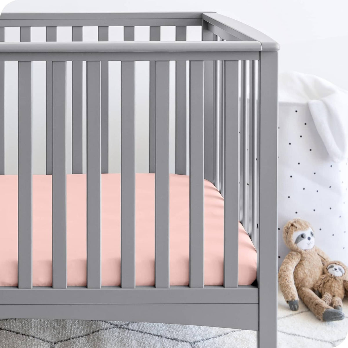 Pink crib fitted sheet on crib mattress, with fitted corners visible over stripes sheet