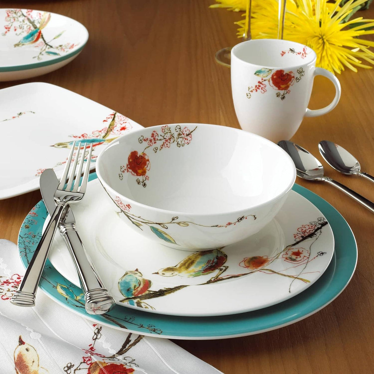 White ceramic bowl and mug with bird-and-floral pattern on teal plate, with cutlery