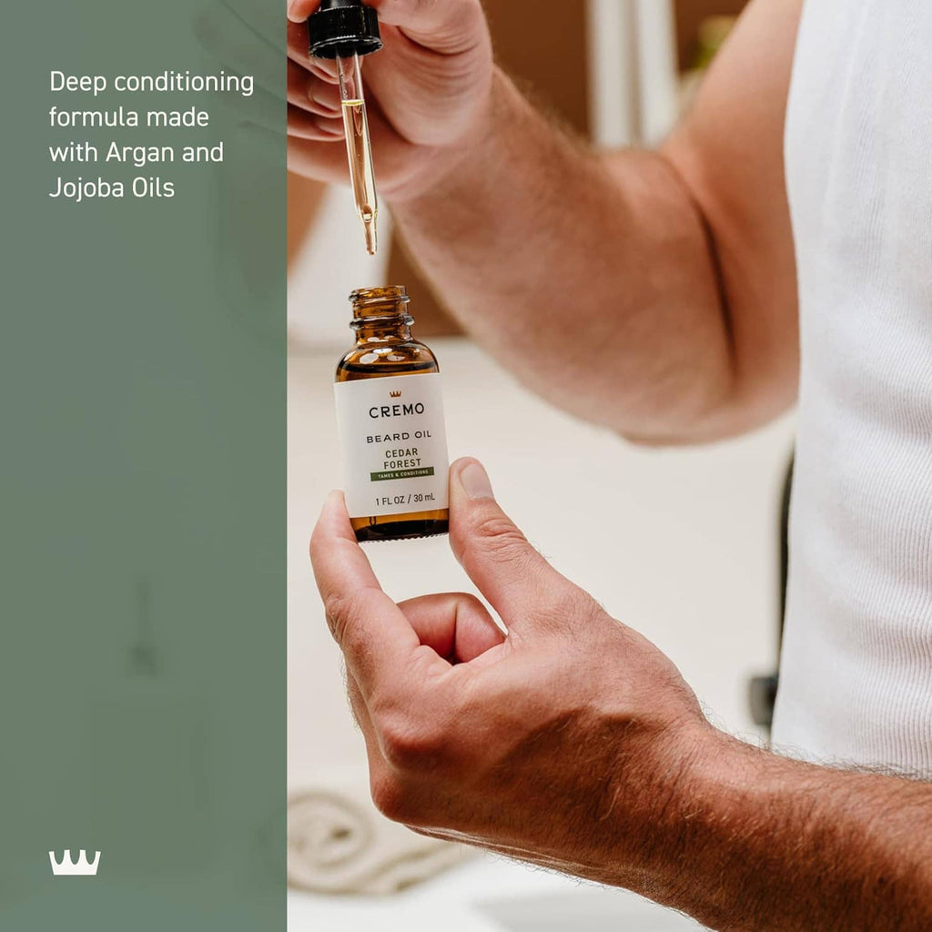 Hand applying Cremo beard oil from dropper over small amber bottle