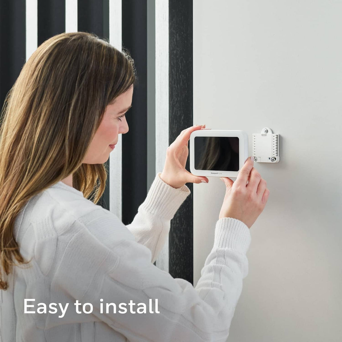 White thermostat mounted on wall as person installs and uses a phone