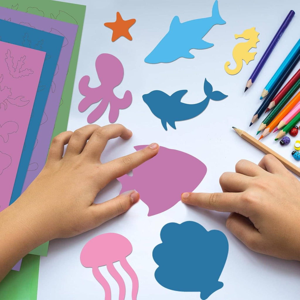 Colorful ocean animal shape cutouts arranged on craft paper with pencils and hands