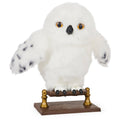 White interactive owl plush with amber eyes, perched on a brown base with gold posts.
