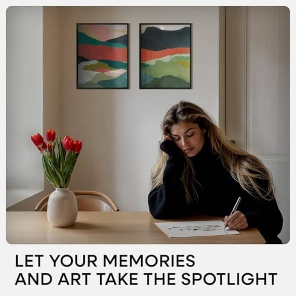 Black picture frames on wall above a desk, woman writing near the artwork