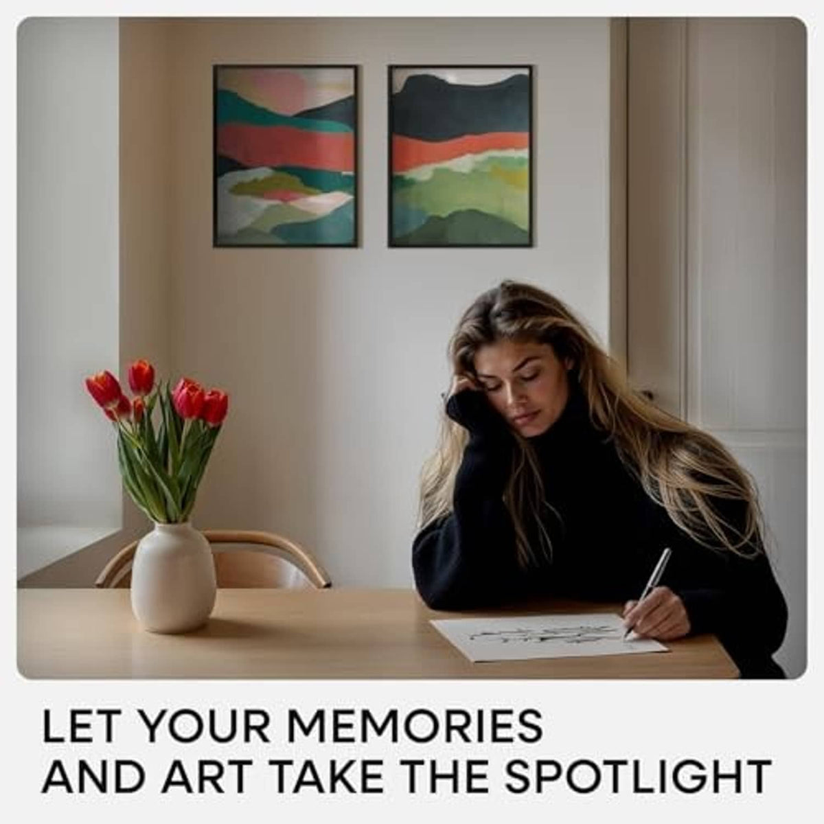 Black picture frames on wall above a desk, woman writing near the artwork