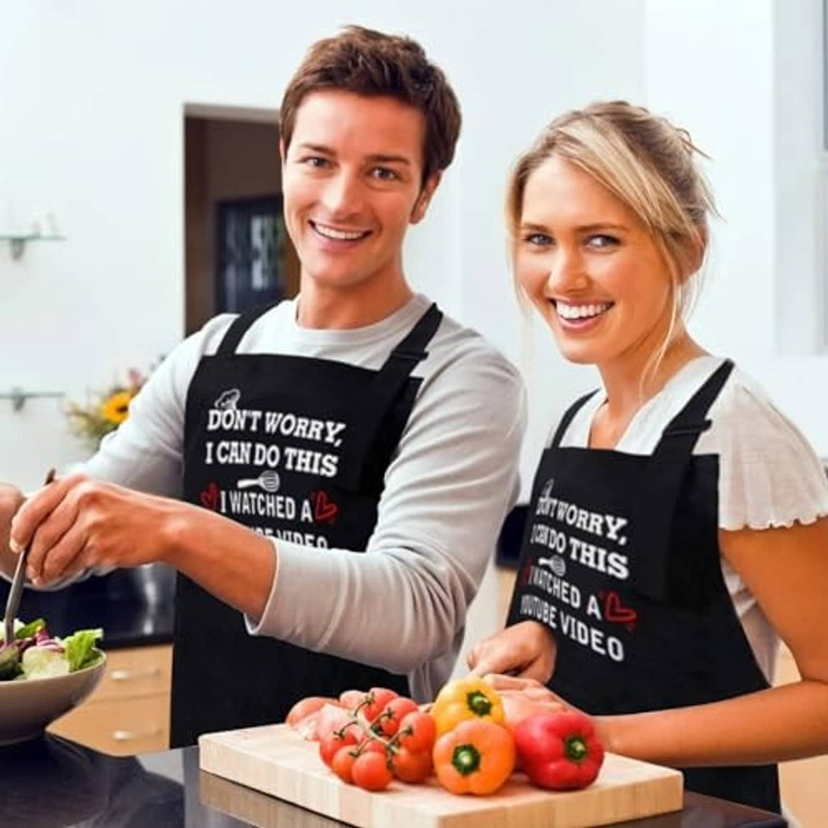 Two people wearing black aprons with the "Don’t Worry, I Can Do This" slogan while cooking.