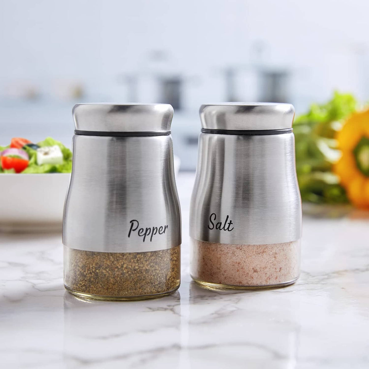 Stainless steel salt and pepper shakers standing side by side with perforated tops.