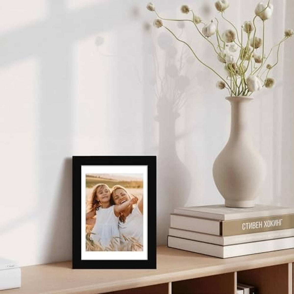 Black 5x7 photo frame standing on a shelf with a family photo behind glass
