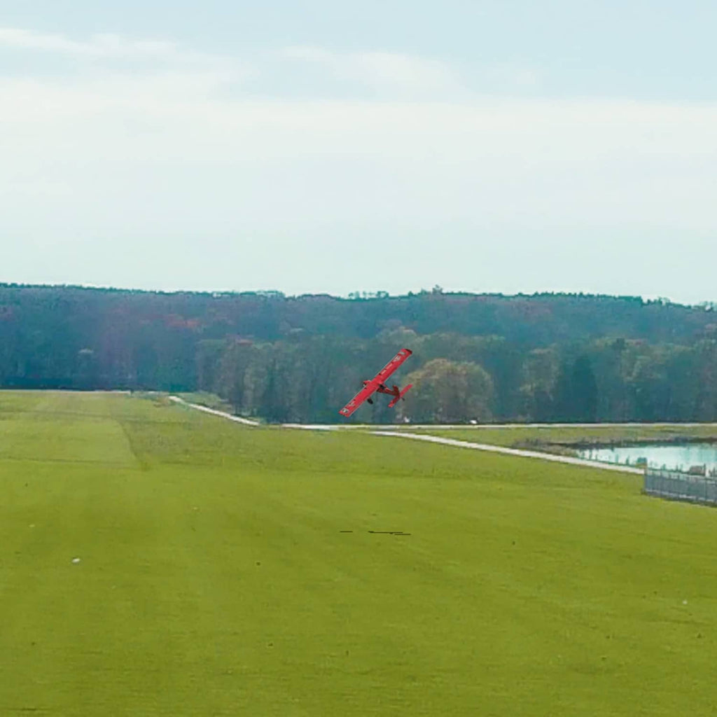 Red RC airplane flying above a green field