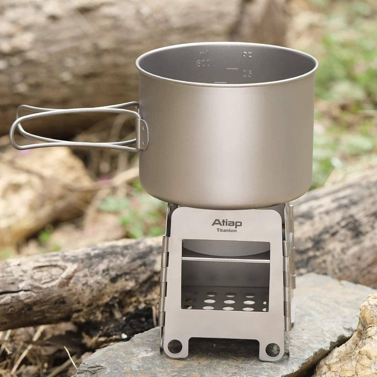 Titanium camping stove with metal pot set on top, front burner tray with hole pattern