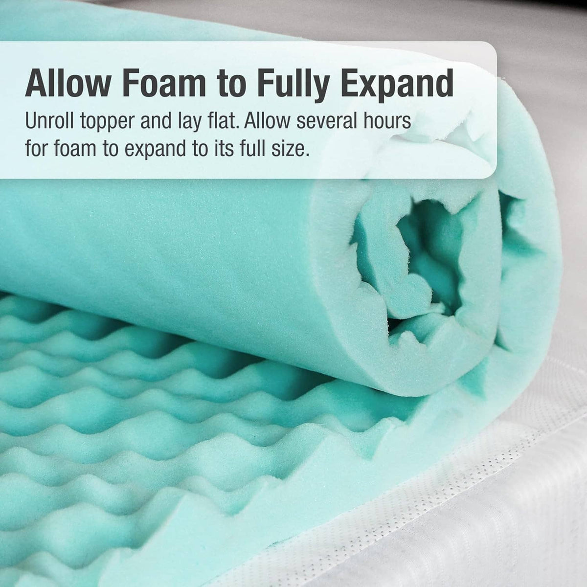 Rolled egg-crate foam mattress topper in light teal expanding to full thickness.