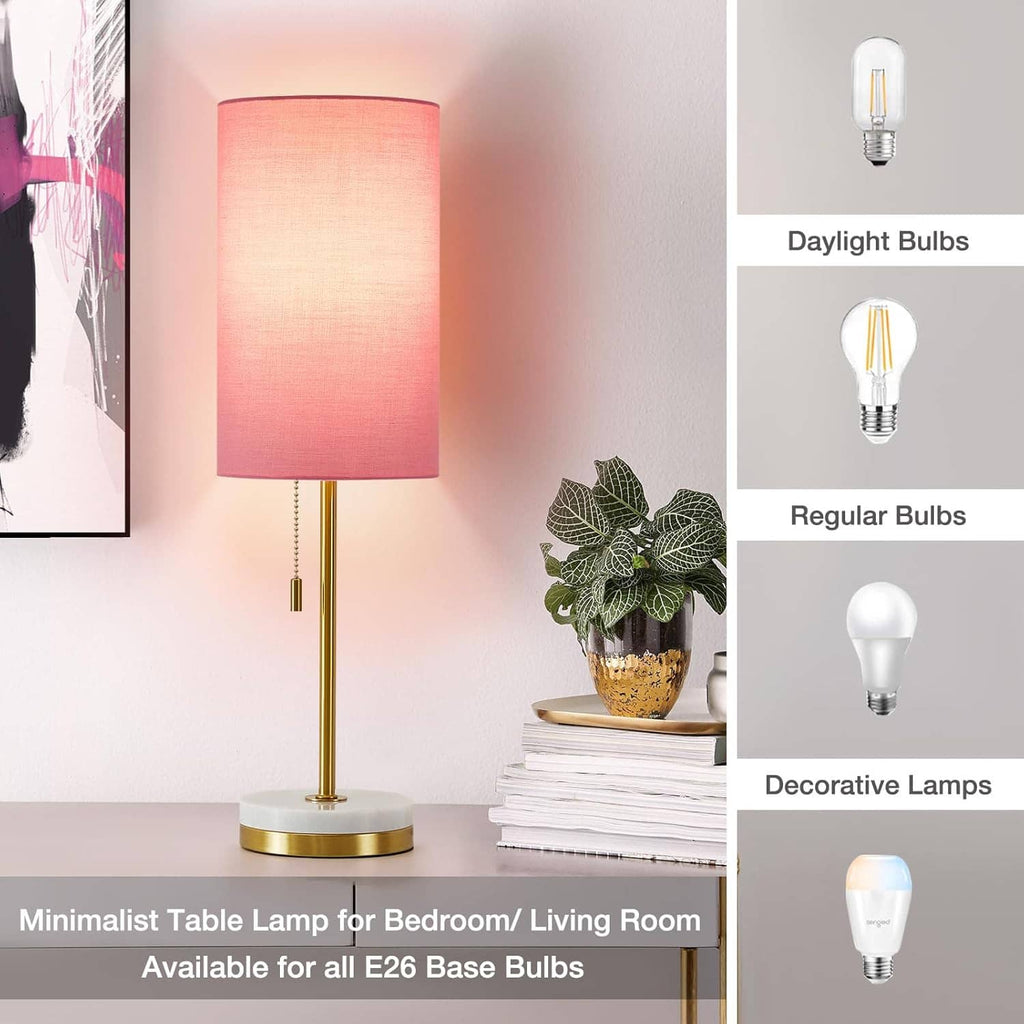 Minimalist table lamp with pink fabric shade, gold stem, and round white base.