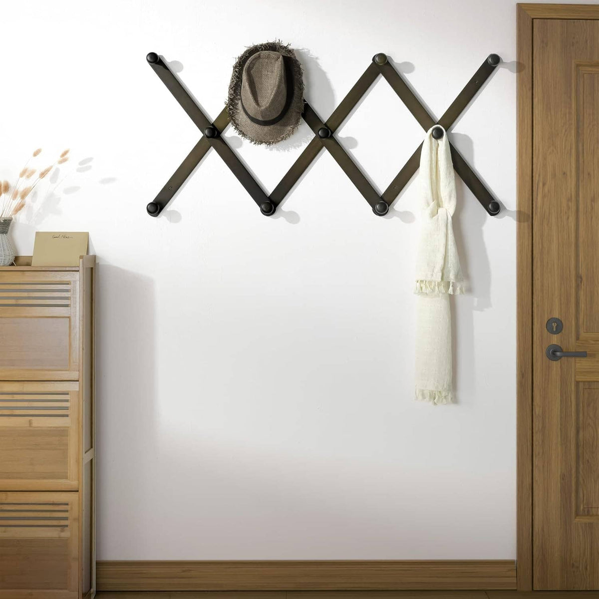 Wall-mounted accordion hat rack with round hooks holding a hat, scarf, and bag