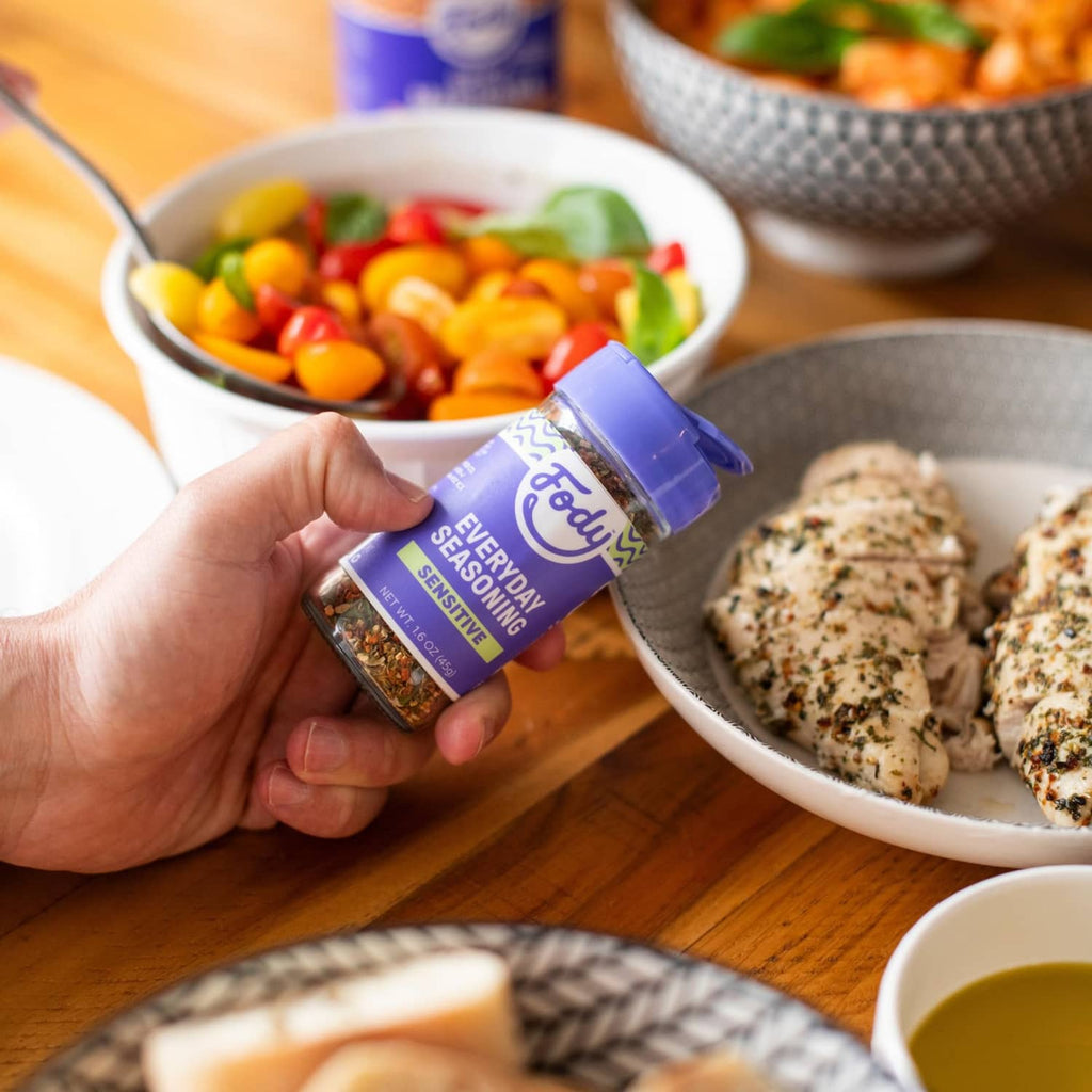 Hand holding Fody Foods sensitive everyday seasoning jar above food bowls