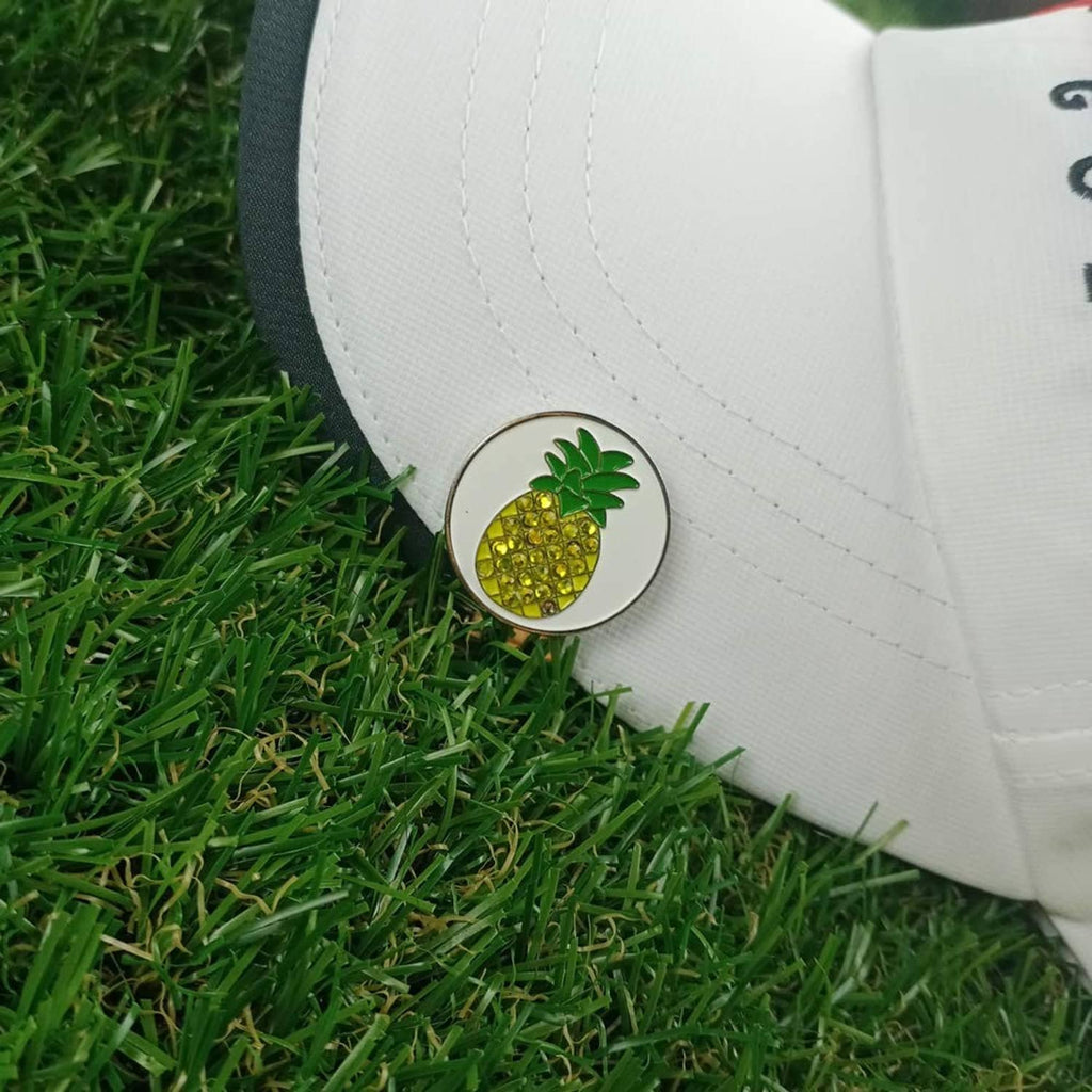 Pineapple golf ball marker clipped to white cap; round metal coin with green leaf art