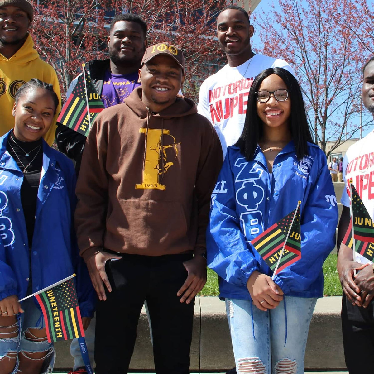 Group holding Juneteenth mini flags with star field, stripes, and “JUNETEENTH” text