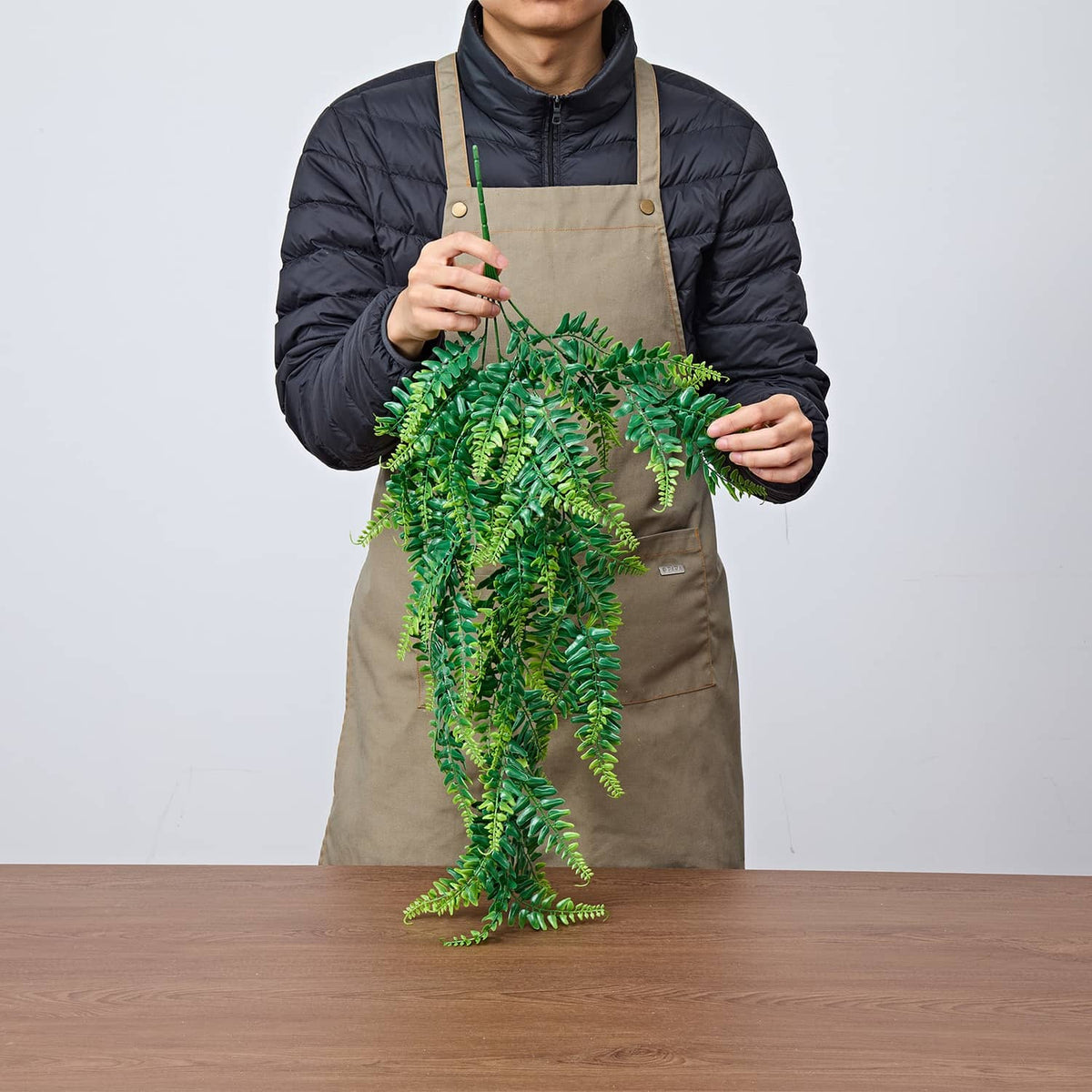 Artificial hanging Boston fern bush held by a person, with dense green fronds