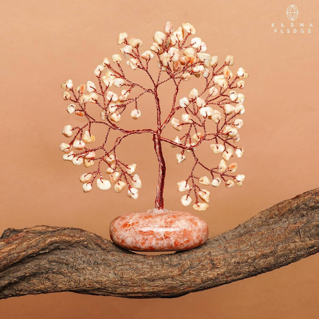 Sunstone crystal tree ornament with red wire branches and orange-pink base on wood