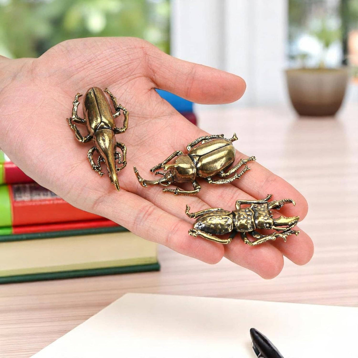 Three brass beetle figurine ornaments on an open hand