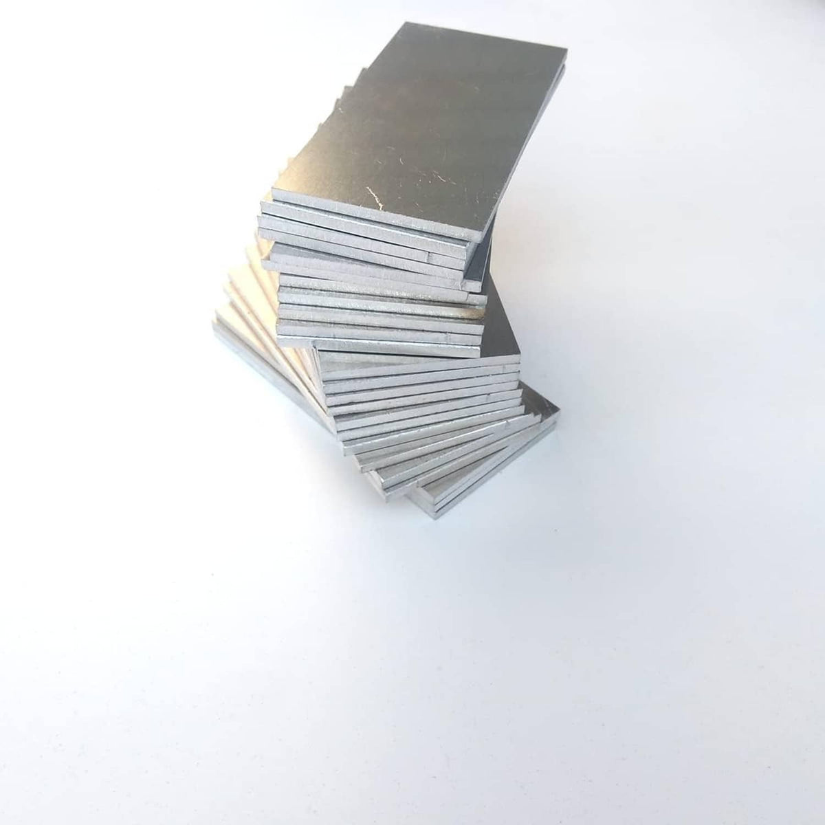 Stack of rectangular silver aluminum coupon plates with visible layered strip edges.