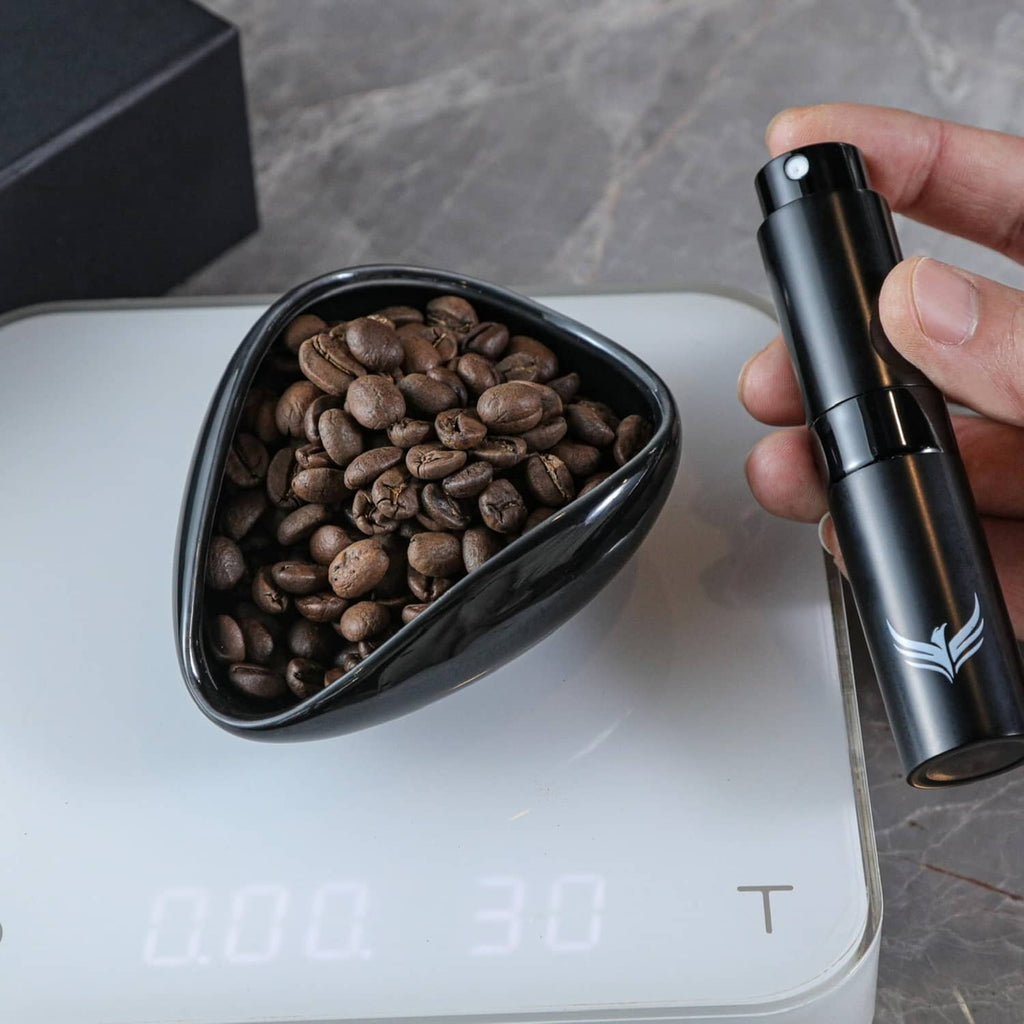Black coffee dosing cup filled with beans next to a black RDT sprayer on a scale