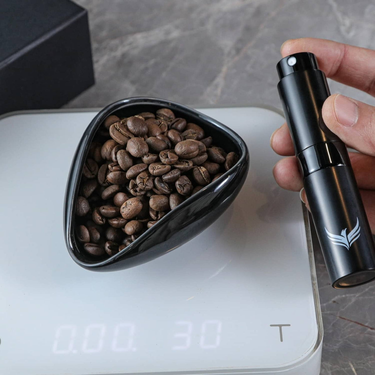 Black coffee dosing cup filled with beans next to a black RDT sprayer on a scale