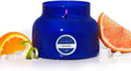 Blue glass jar candle with metal lid, flame visible, citrus slices beside the jar