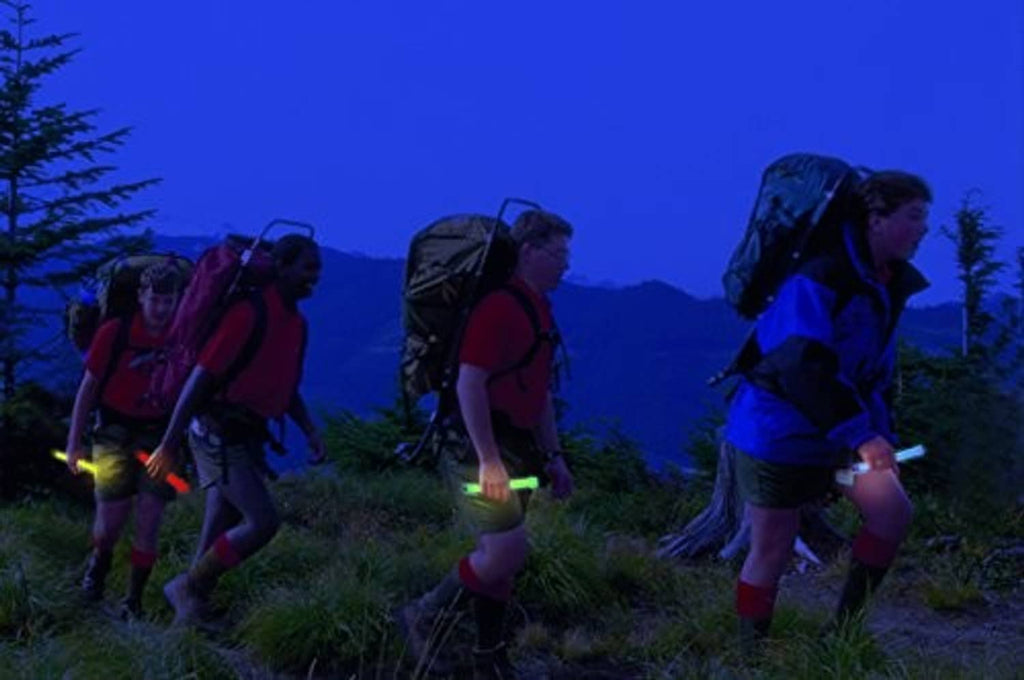 Group of hikers holding green glow sticks outdoors for visibility at night