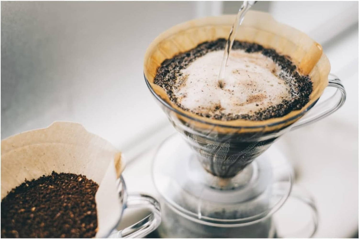 V60 paper coffee filter with dark grounds and hot coffee being poured