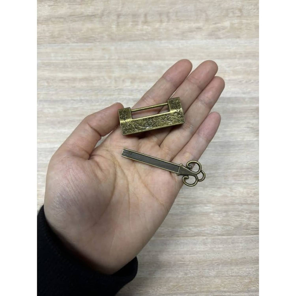 Bronze padlock body with matching key, held in a hand for scale