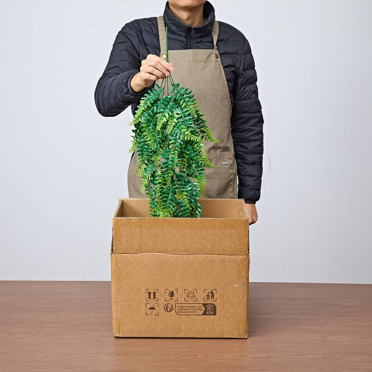 Artificial hanging Boston fern bush being unpacked from a cardboard box