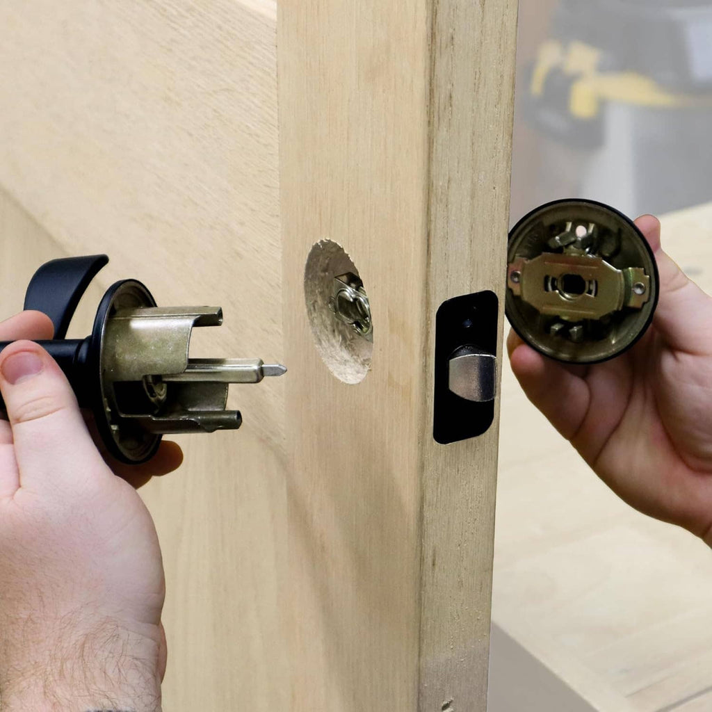 Hands fitting a door lock cylinder and latch into holes on a wooden door