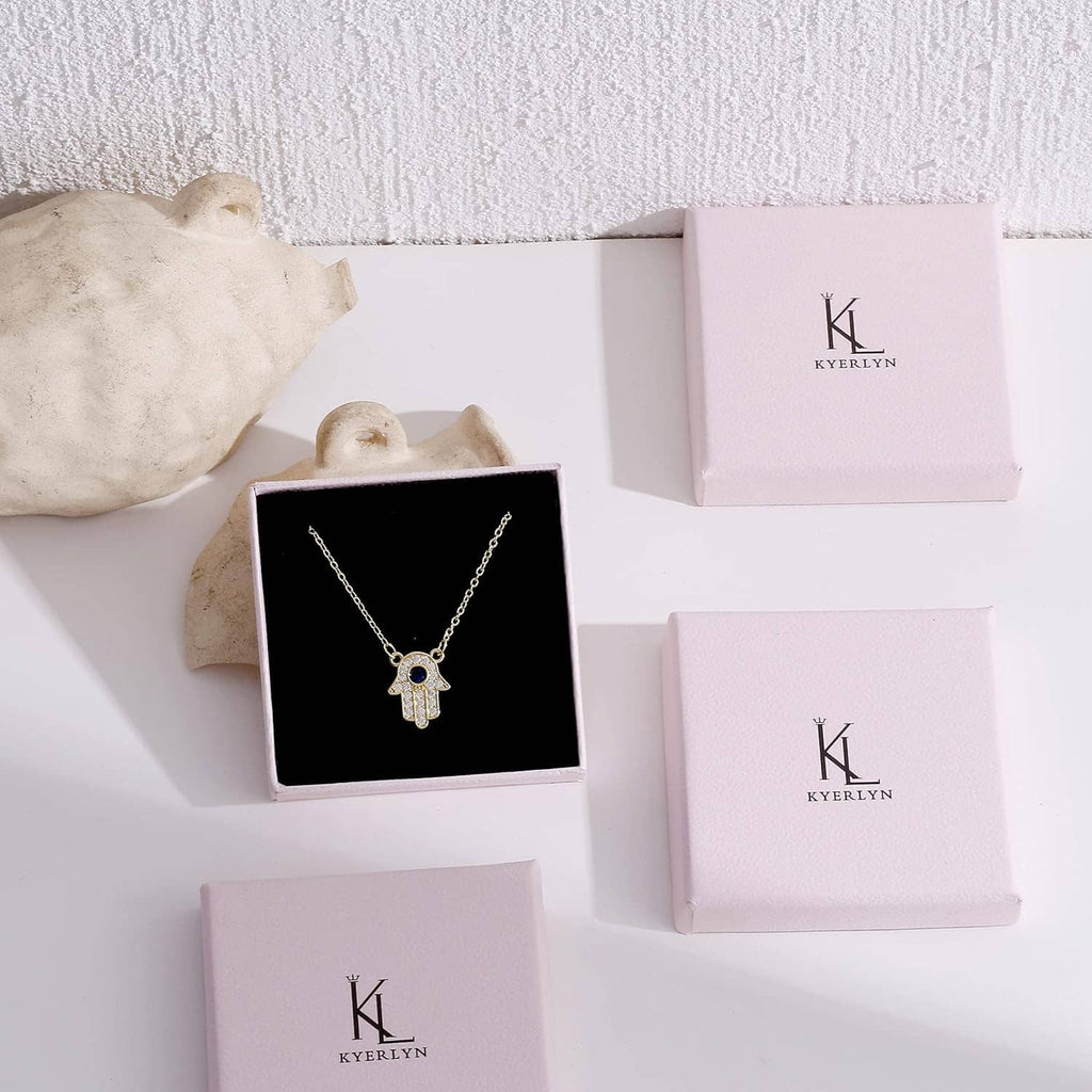 Gold charm necklace on black jewelry display card with Kyerlyn boxes
