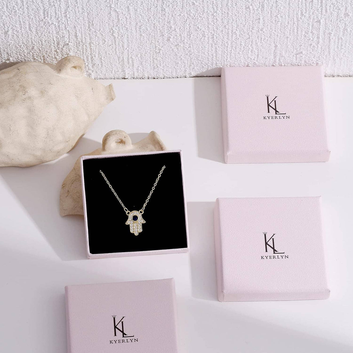 Gold charm necklace on black jewelry display card with Kyerlyn boxes