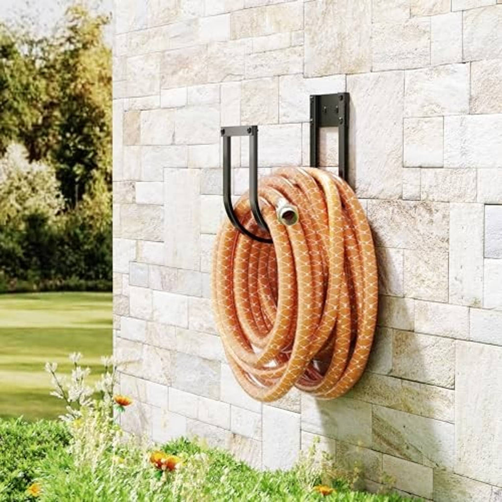 Black metal wall-mounted hose hanger holding coiled orange striped hose on stone wall