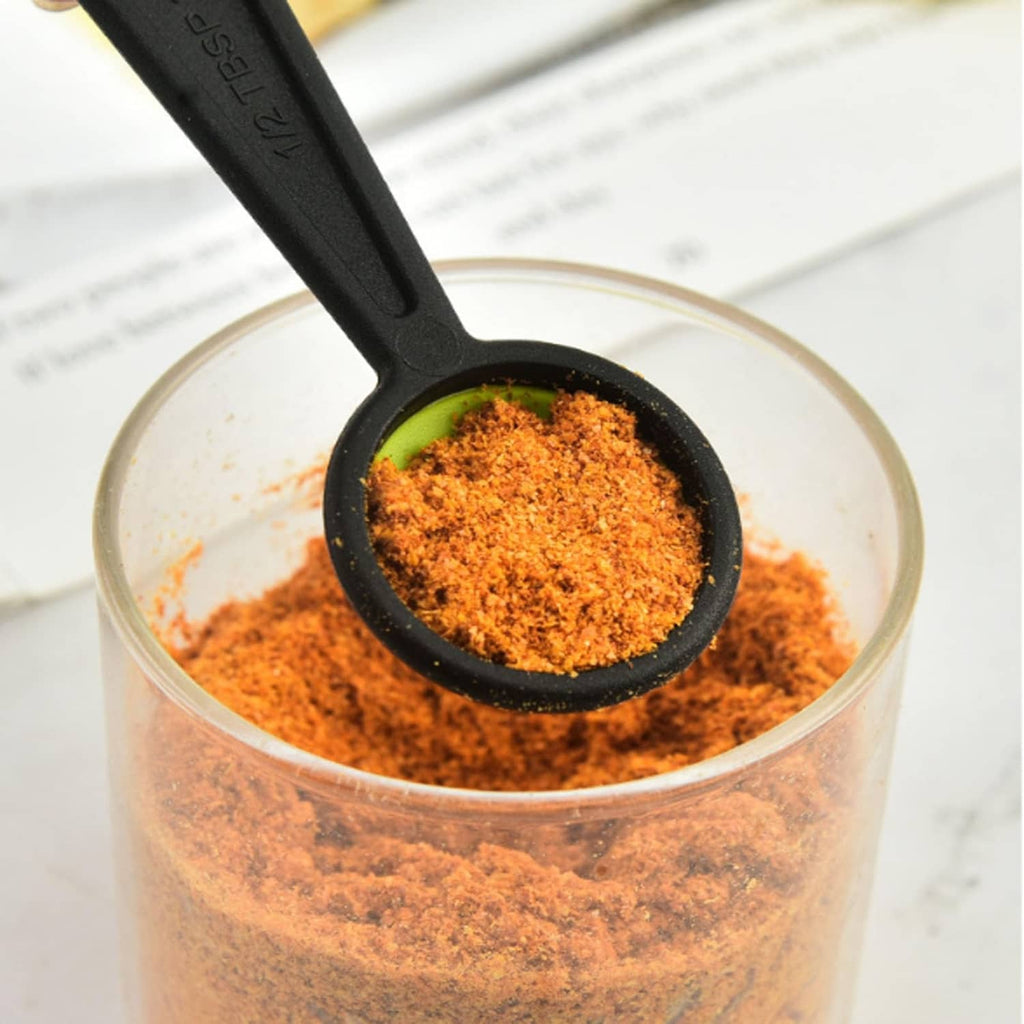 Small black silicone measuring spoon filled with orange seasoning over a clear bowl