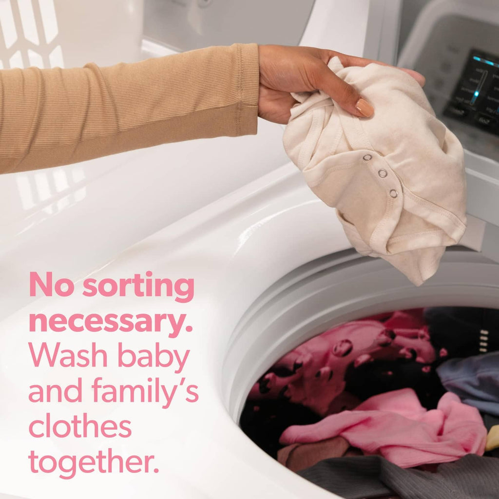 Hand placing a white baby onesie into a washing machine drum