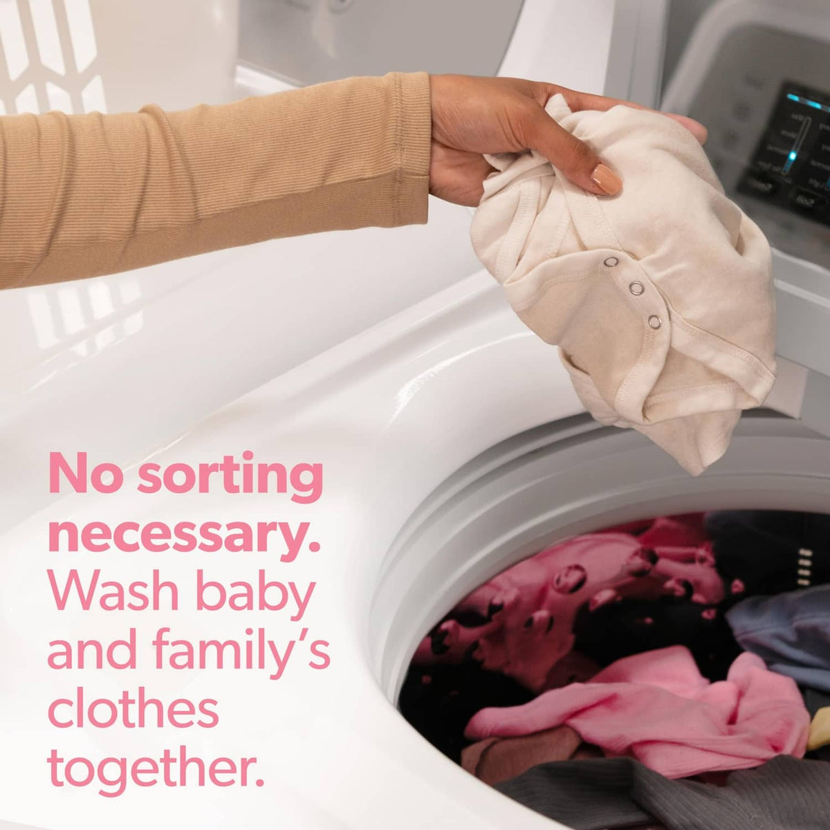 Hand placing a white baby onesie into a washing machine drum