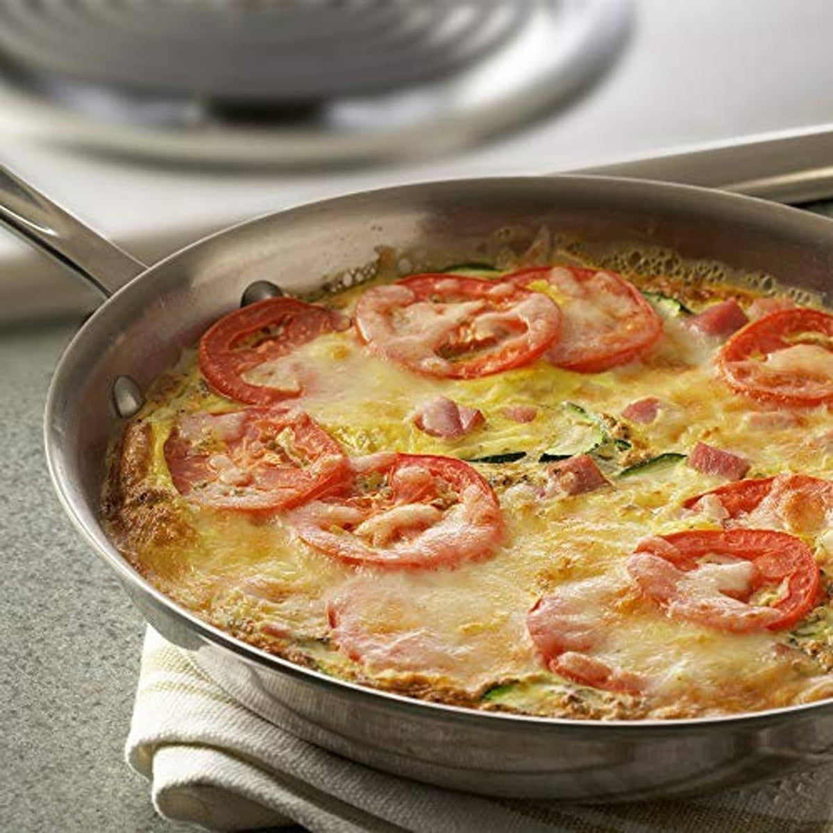 Baked casserole in a skillet with melted cheese, tomatoes, and herbs