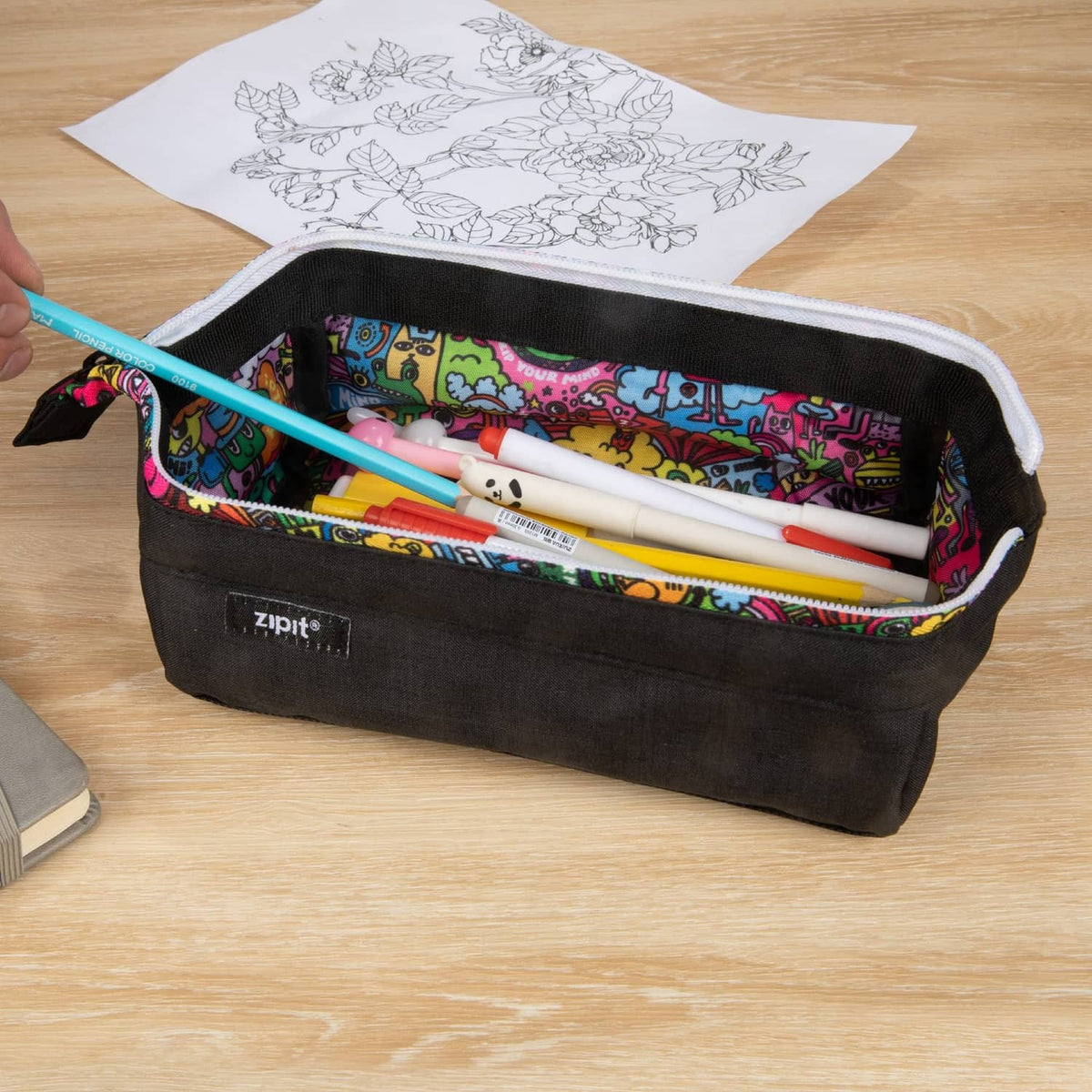 Black ZIPIT pencil case open with colorful doodle lining and pens and markers inside