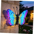 Solar LED butterfly wall decor with multicolor glowing wings, hanging on stone wall