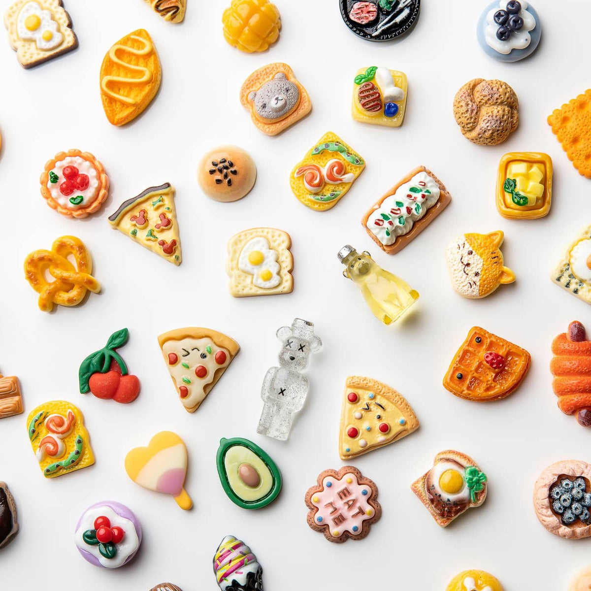 Assorted resin food charms on white layout, including pizza slices, pastries, hearts, and snacks