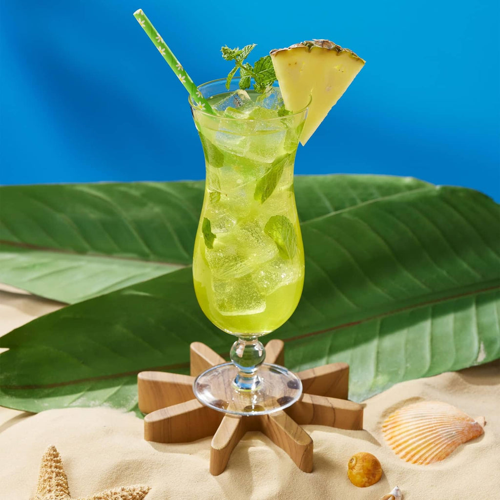 Green cocktail in stemmed glass with mint and pineapple garnish