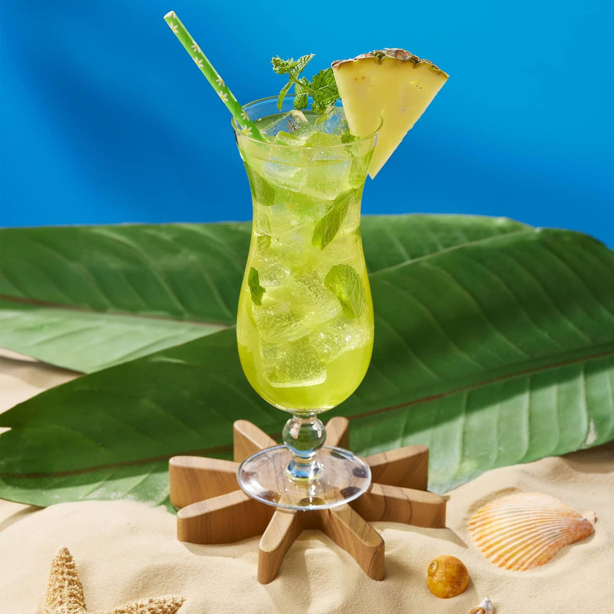 Green cocktail in stemmed glass with mint and pineapple garnish