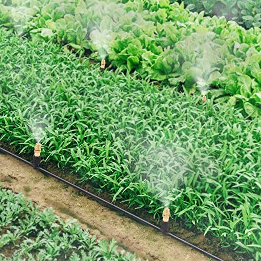 Brass atomizing nozzles along black irrigation tubing watering a green garden bed